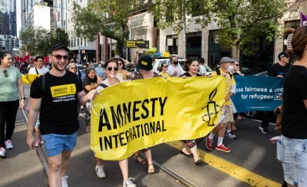 A group of people at a march holding a black and yellow Amnesty International banner between them