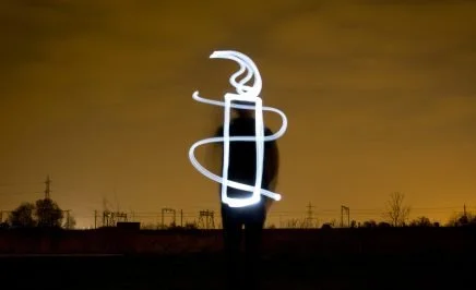 Amnesty Candle - light drawing. A light artist stands against a dark night sky and paints the AI candle.