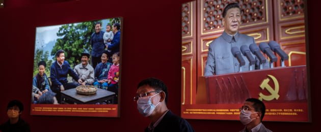 Party members in China stand in front of an image of Xi Jinping
