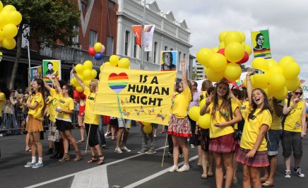 A group of activists in yellow t-shirts hold signs and balloons at a rally