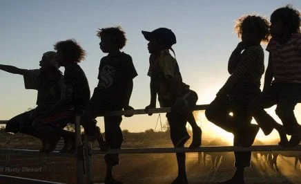 Indigenous children are silhouetted against the sunset as they sit on a fence