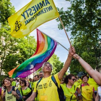 Amnesty International activists take part in Pride march, waving Amnesty and Pride flags.