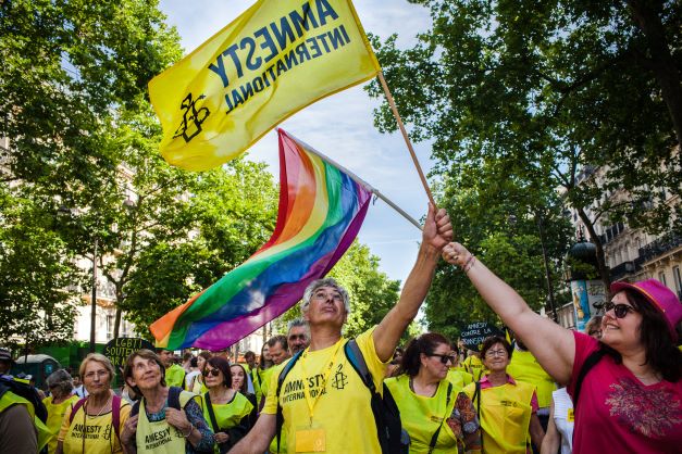 Amnesty International activists take part in Pride march, waving Amnesty and Pride flags.
