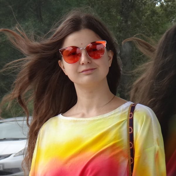 Yulia Tsvetkova smiling, wearing red sunglasses and a rainbow long sleeve top