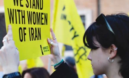 Woman at protest holding sign that says 'We stand with women of Iran'.
