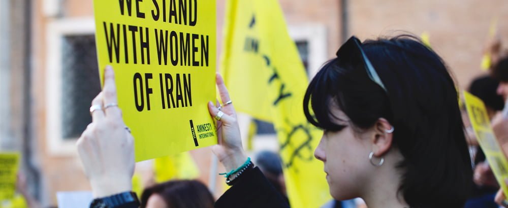 Woman at protest holding sign that says 'We stand with women of Iran'.