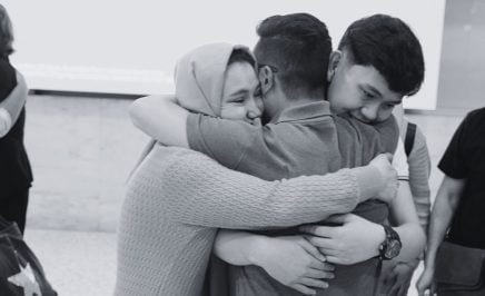 A family of three embrace at an airport