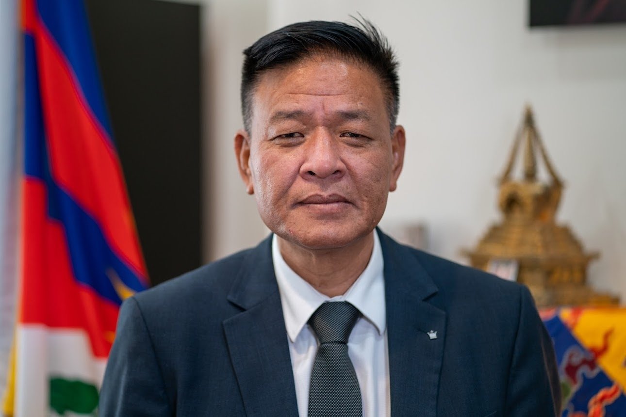 A photo of Penpa Tsering, a Tibetan man with dark hair, in a suit sitting at a desk.