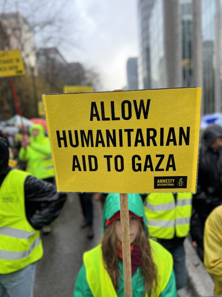 A demonstrator holds a yellow sign with the message "ALLOW HUMANITARIAN AID INTO GAZA".
