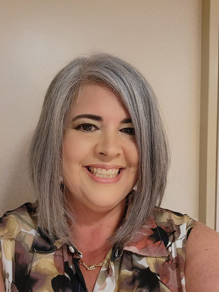 A woman in a floral shirt with grey hair smiles at the camera.