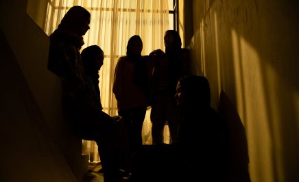 Afghan women pose for a portrait indoors in a darkened room.