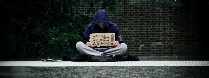 homeless man in a hoodie holding a sign