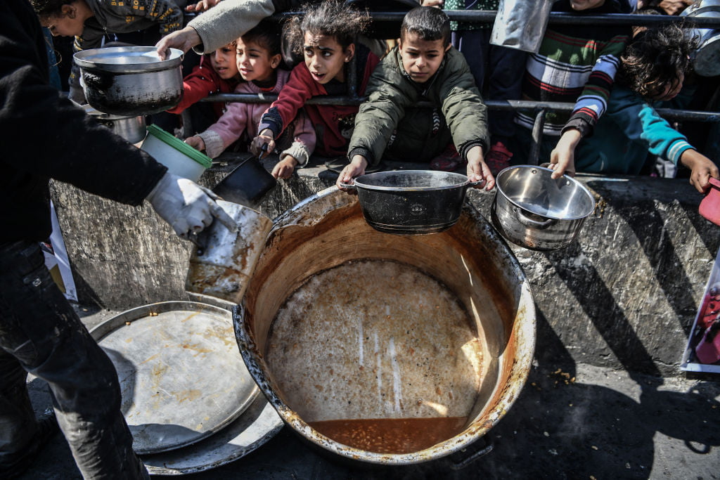 Palestinians hold out containers after waiting in long queues for food in Rafah, as aid organisations struggle to meed demand. 