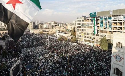 TOPSHOT - A Syrian flag flutters above crowds gathering during celebrations marking one year since a lightning Islamist-led offensive that eventually toppled the country's longtime ruler, in central Hama on December 5, 2025. (Photo by OMAR HAJ KADOUR / AFP via Getty Images)