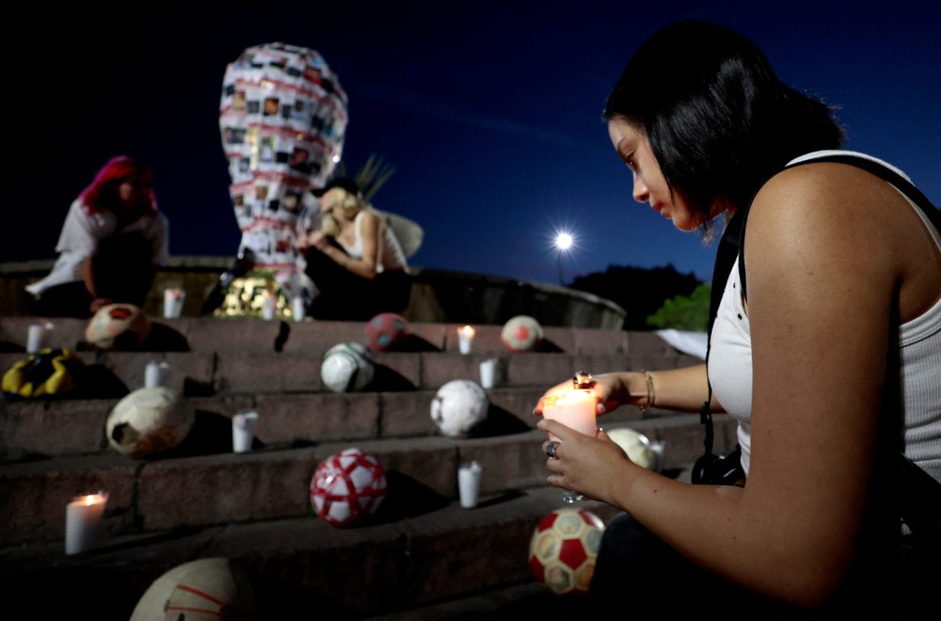 A student from the Jesuit University of Guadalajara (ITESO) places a candle near a replica of the FIFA World Cup trophy decorated with pictures of missing persons, during an art intervention with the 