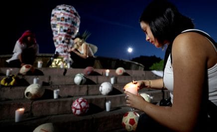 A student from the Jesuit University of Guadalajara (ITESO) places a candle near a replica of the FIFA World Cup trophy decorated with pictures of missing persons, during an art intervention with the 