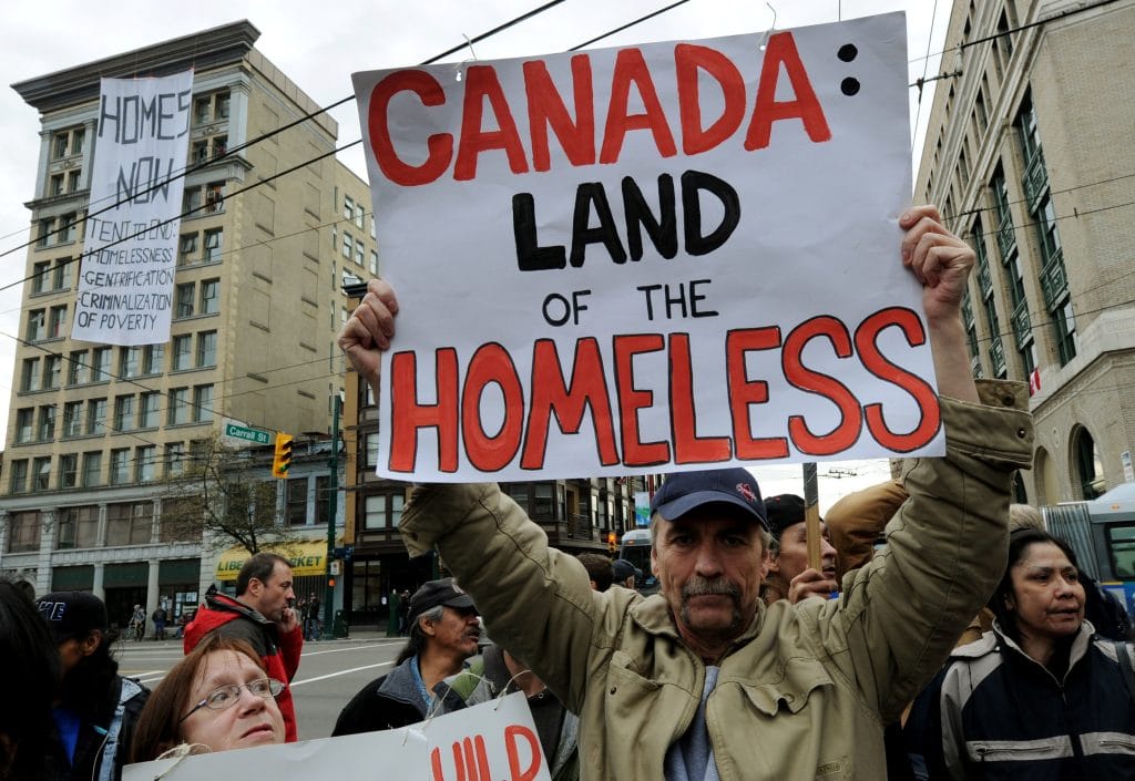A man protests against homelessness near the newly opened Olympic Tent Village which will house the homeless in donated tents as a protest against the Winter Olympics in the Eastside area of Vancouver on February 15, 2010. Canada is spending over two billion dollars on the Winter Olympics but just steps away from the venue for the opening ceremony sits one of the country's most notorious slums where drug addiction and prostitution are rife. The scenes of homelessness and the squalor of Downtown Eastside are not the images Olympic organizers want visitors to leave with. But the neighbourhood's close proximity to BC Place Stadium where the Olympic cauldron will be lit on Friday, will make it hard for visitors to miss. AFP PHOTO/Mark RALSTON (Photo by MARK RALSTON / AFP via Getty Images)