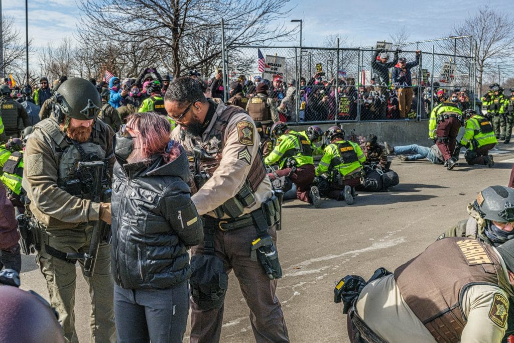 Hennepin County sheriff's deputies detain a demonstrator outside the Bishop Henry Whipple Federal Building during a protest opposing US Immigration and Customs Enforcement (ICE) operations, in Minneapolis, Minnesota, on March 1, 2026. The demonstration was organized in connection with a prayer camp established across the street at the sacred site of Mni Owe Sni (Coldwater Spring), where Indigenous organizers have been gathering in recent weeks to pray for families affected by immigration enforcement and to call for "ICE out" and "Land Back." Indigenous leaders say immigration enforcement and detention echo historic patterns of displacement and incarceration experienced by Native communities. The camp at Mni Owe Sni considered a sacred Dakota site was established to center ceremony, prayer and solidarity with immigrant families. (Photo by Kerem YUCEL / AFP via Getty Images)